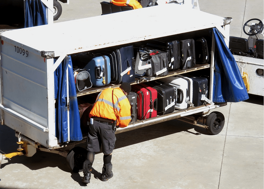 a person in a yellow vest and shorts standing next to a cart full of luggage