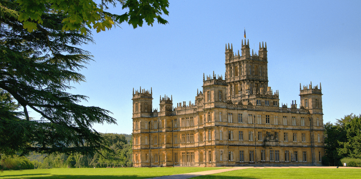 a large stone building with towers and a lawn with Highclere Castle in the background