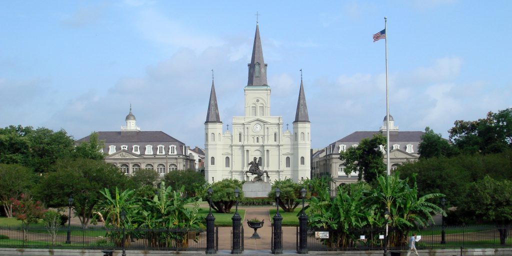 a white building with a clock tower and a statue in front of it with Jackson Square in the background