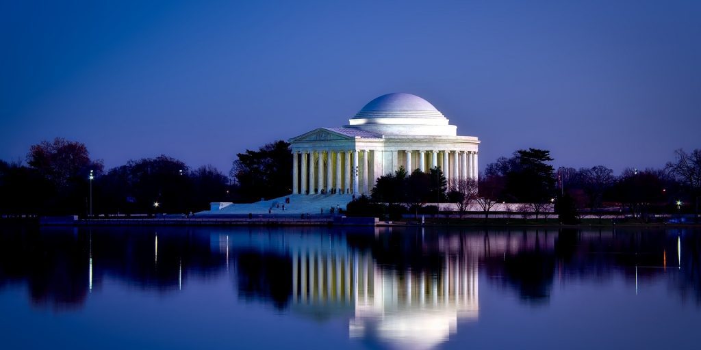 a white building with columns and a dome on the side of it with Jefferson Memorial in the background