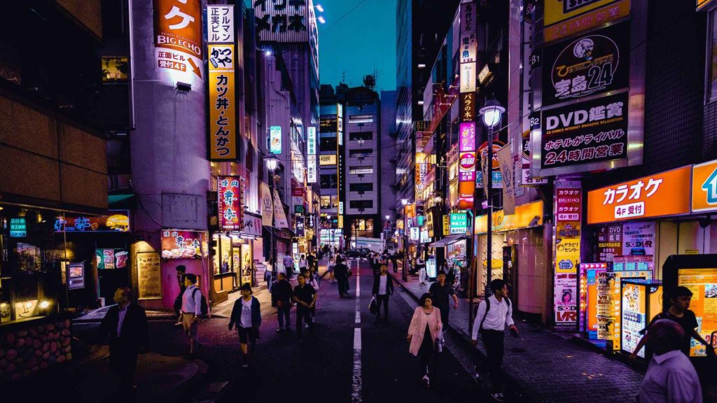 a group of people walking down a street with signs with Kabukichō, Tokyo in the background