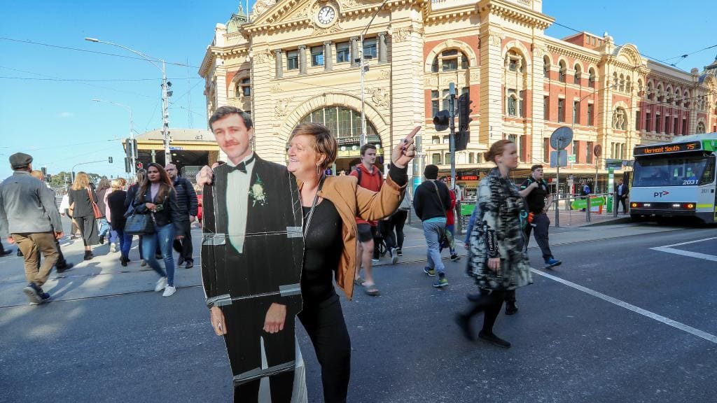 a woman holding a cardboard cutout of a man and a man in a suit