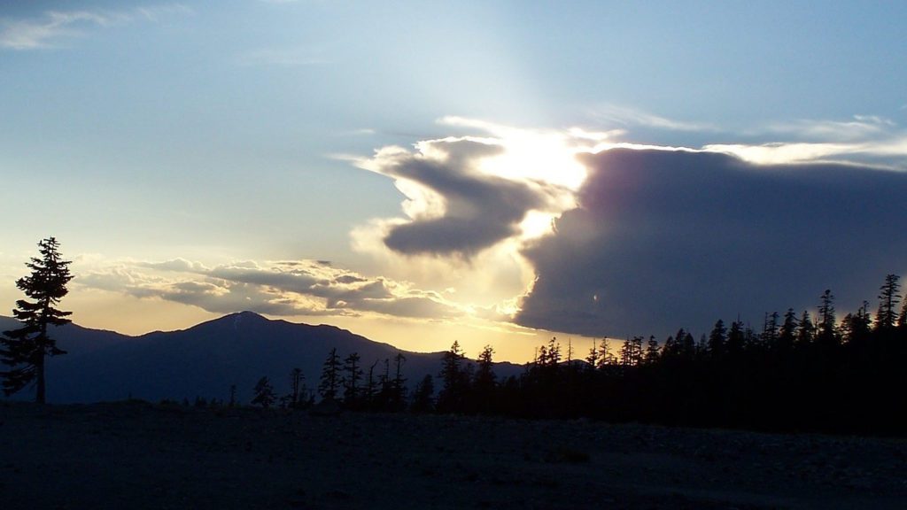 sun shining through clouds over a mountain range