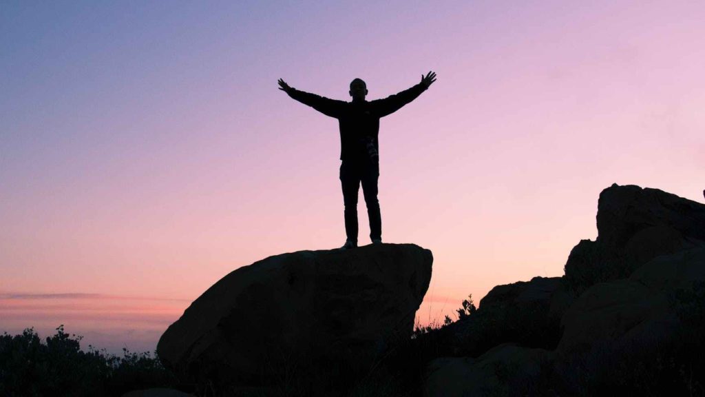 a silhouette of a man standing on a rock with his arms raised