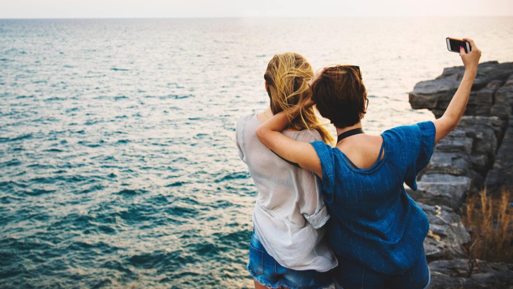 two women standing on a cliff looking at the ocean