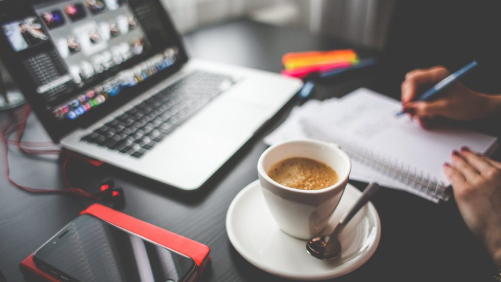 a cup of coffee on a saucer next to a laptop