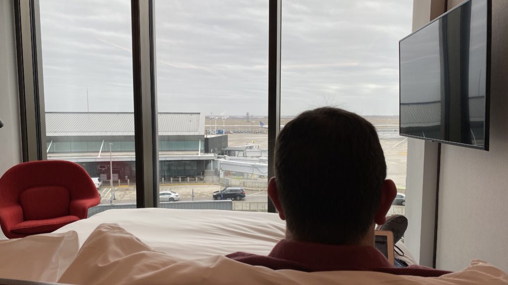 a man sitting on a bed looking out a window at an airport