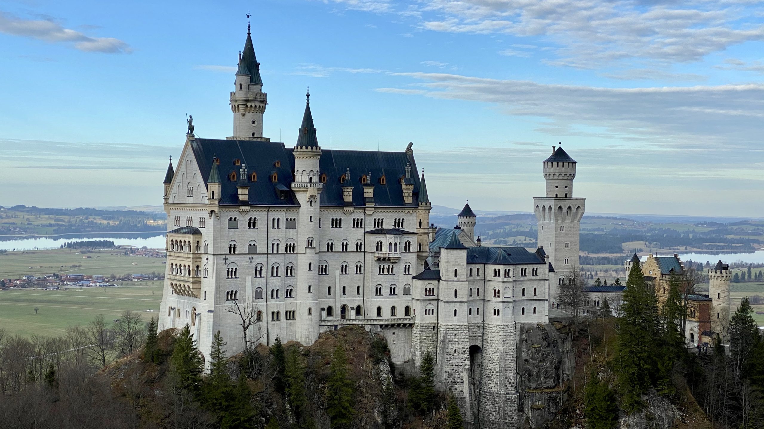 a large white castle on a cliff with Neuschwanstein Castle in the background