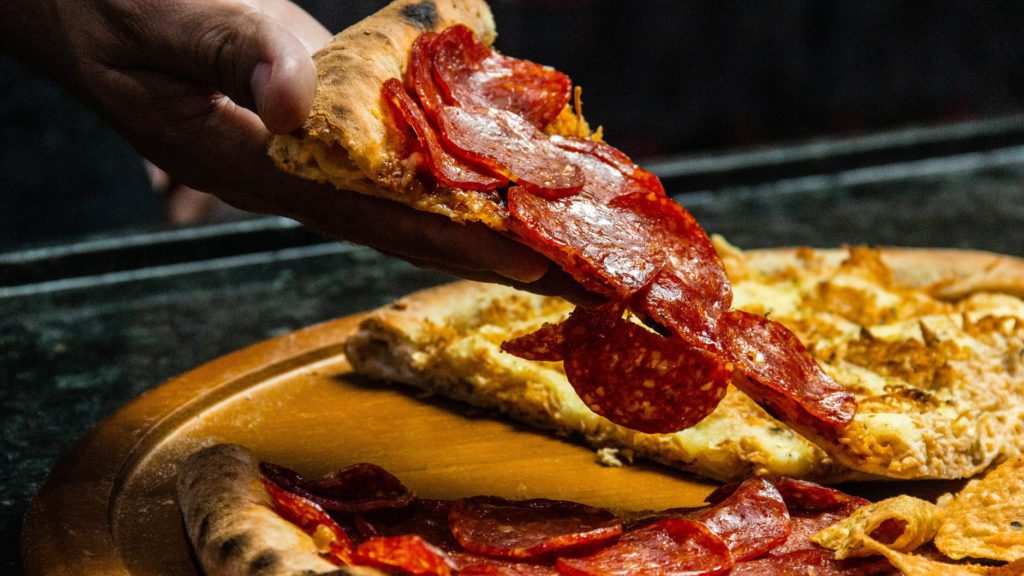 a person holding a slice of pepperoni pizza