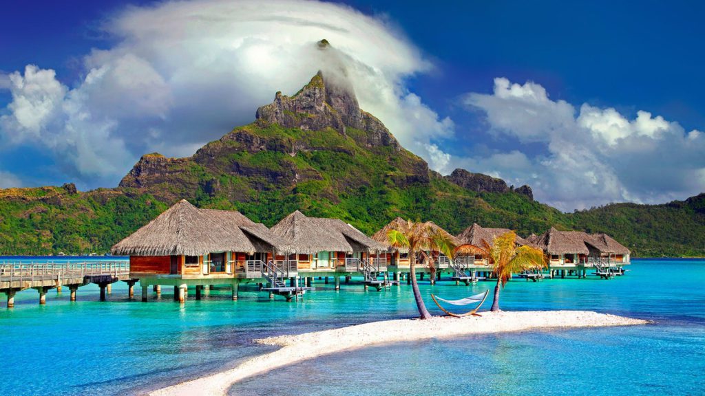 a group of huts on water with Bora Bora in the background