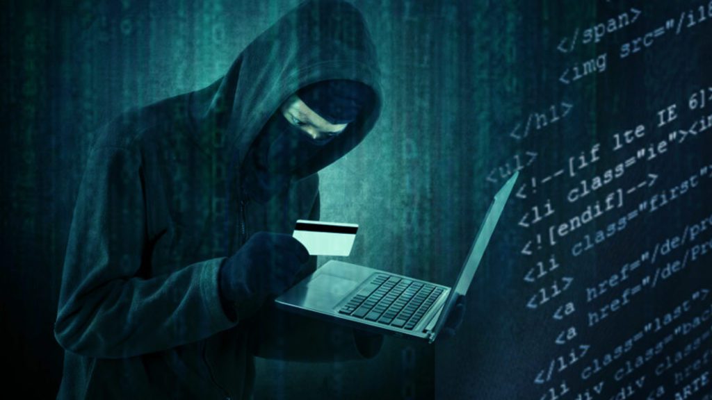 a man in a hood holding a laptop and a credit card