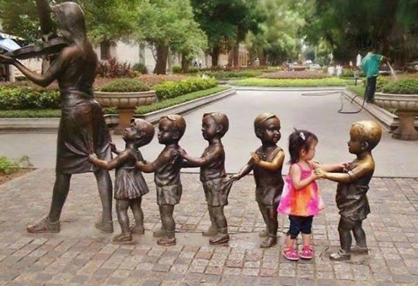 a group of children holding hands in a line of statues