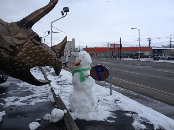 a snowman with a helmet and a shield on the side of the road