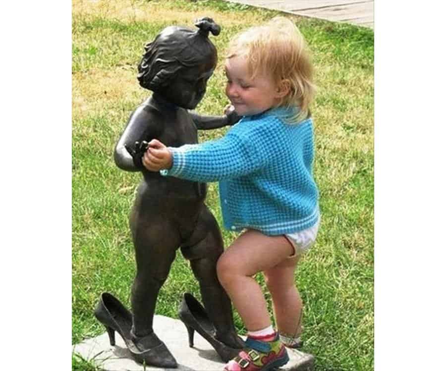 a baby touching a statue of a girl