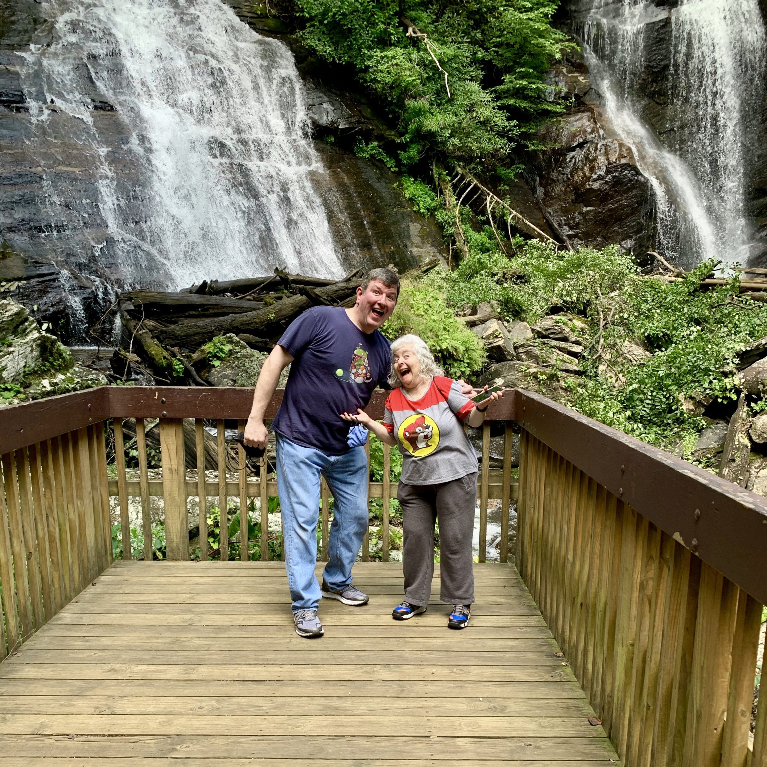 a man and woman standing on a wooden deck with a waterfall in the background