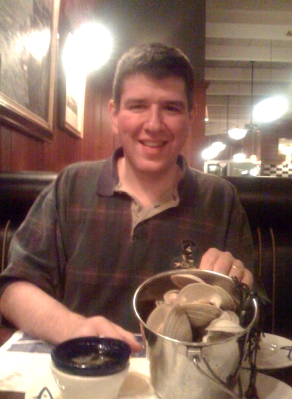 a man sitting at a table with a bucket of clams