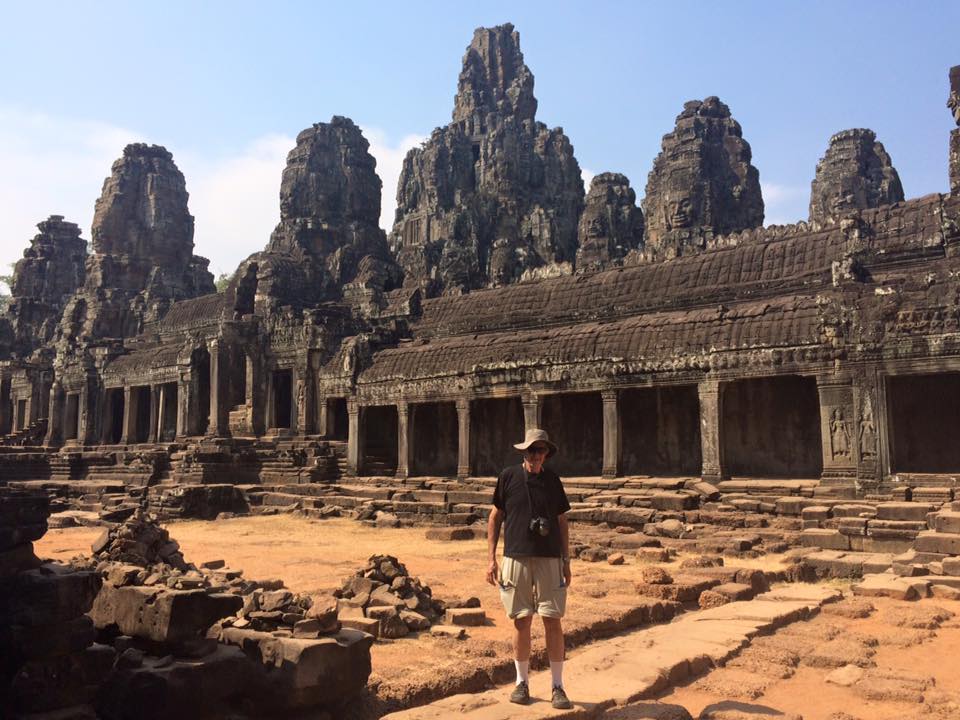 a man standing in front of a stone building with Angkor Wat in the background