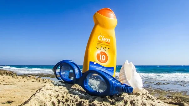a bottle of suntan lotion and swimming goggles on sand