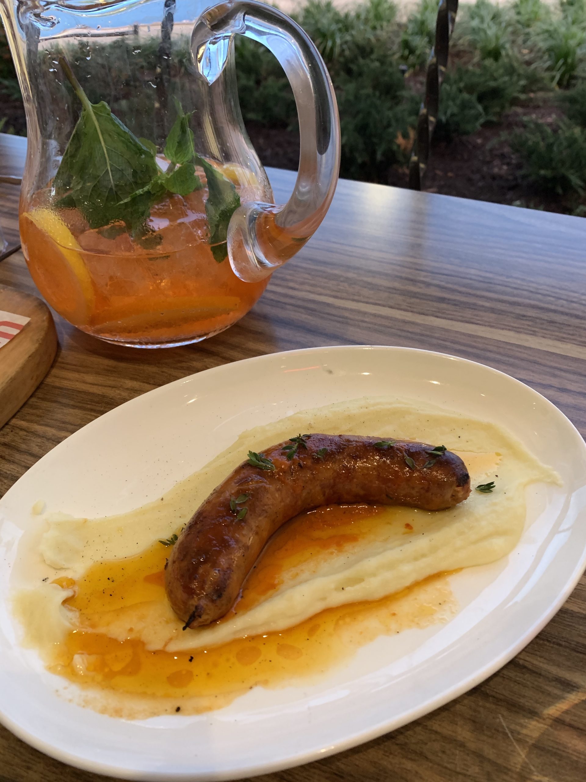 a sausage on a plate with mashed potatoes and a drink