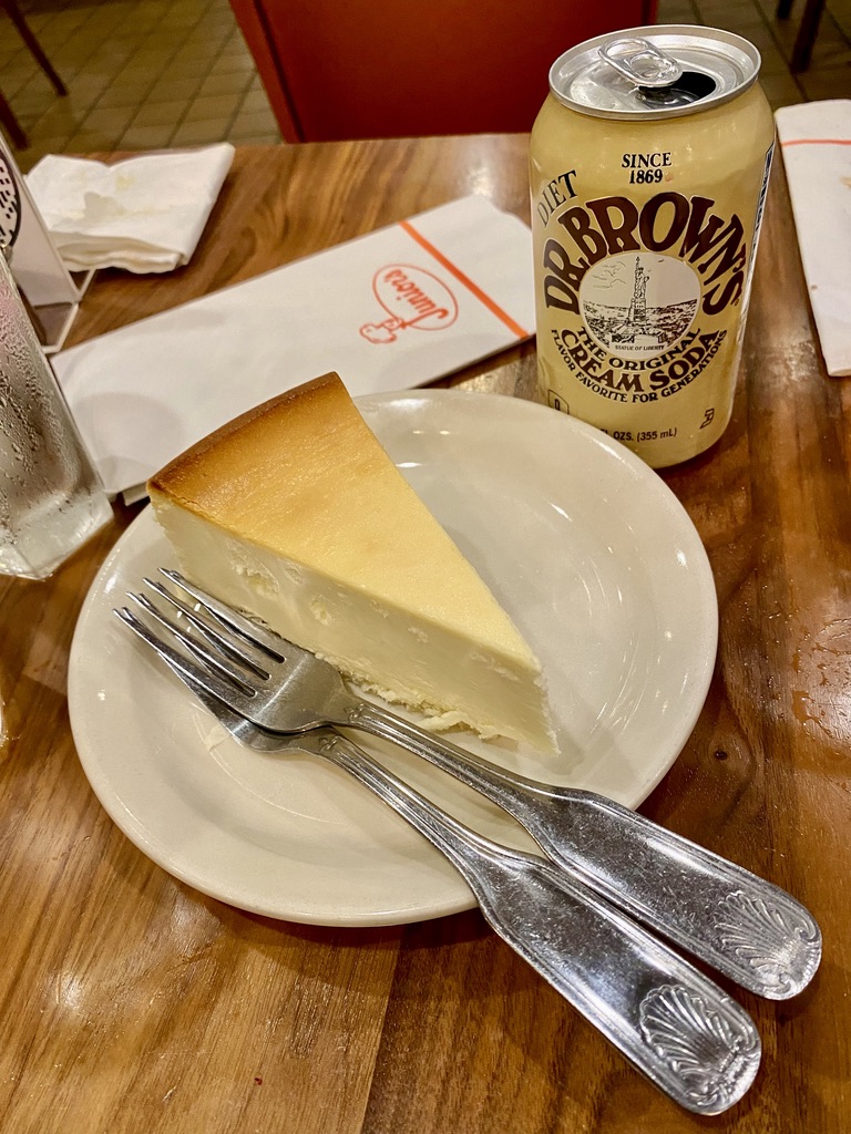 a slice of cheesecake on a plate with a drink and a can