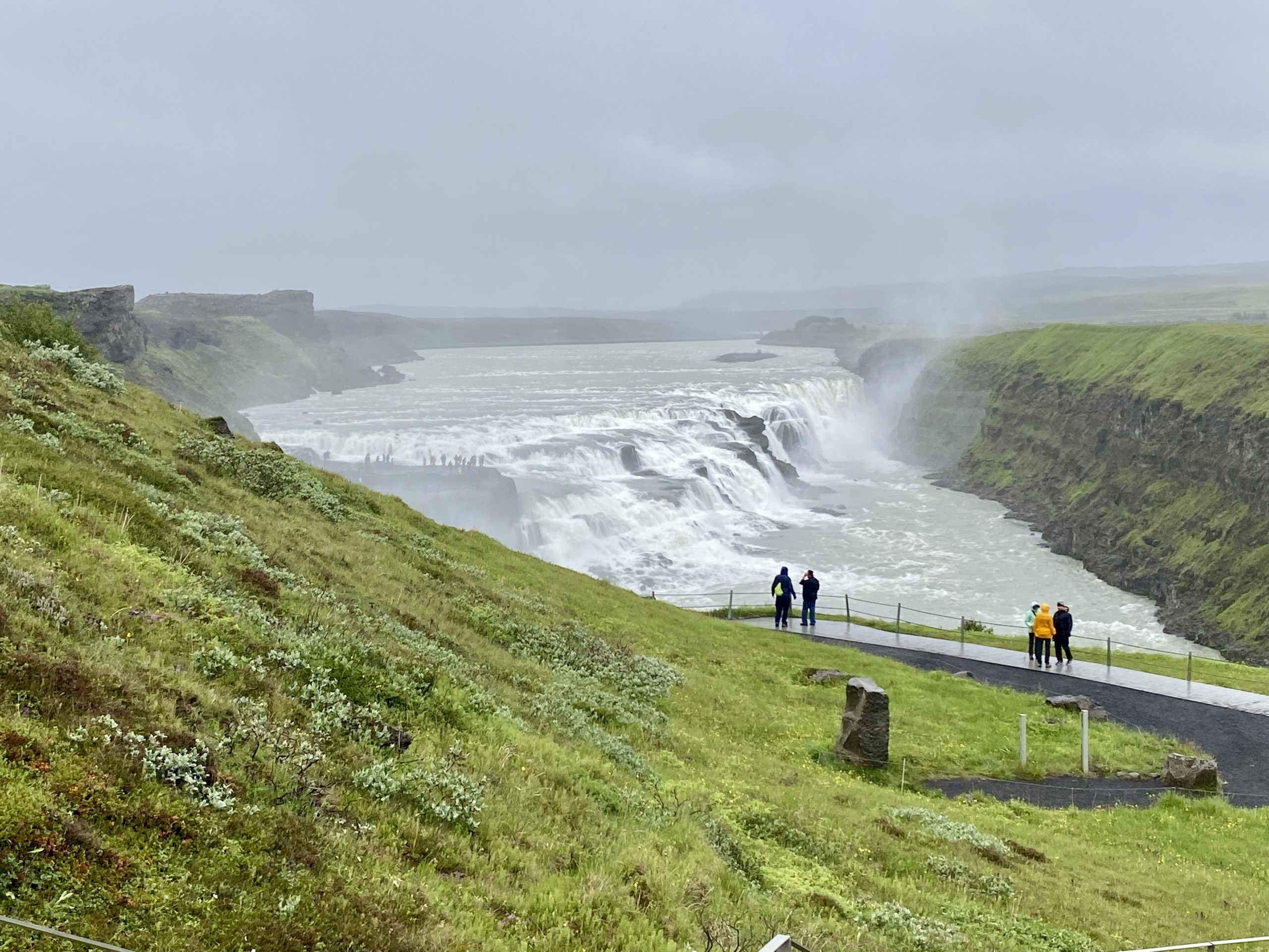 a group of people walking on a path near a waterfall