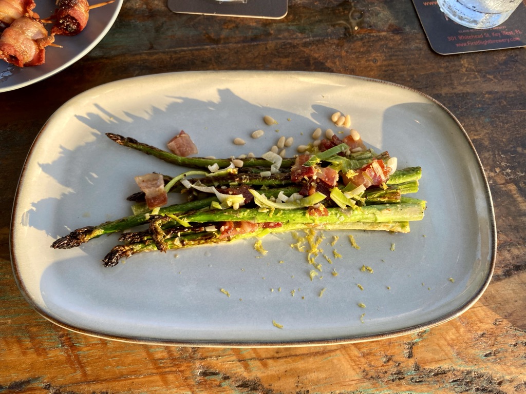 a plate of asparagus with bacon and pine nuts