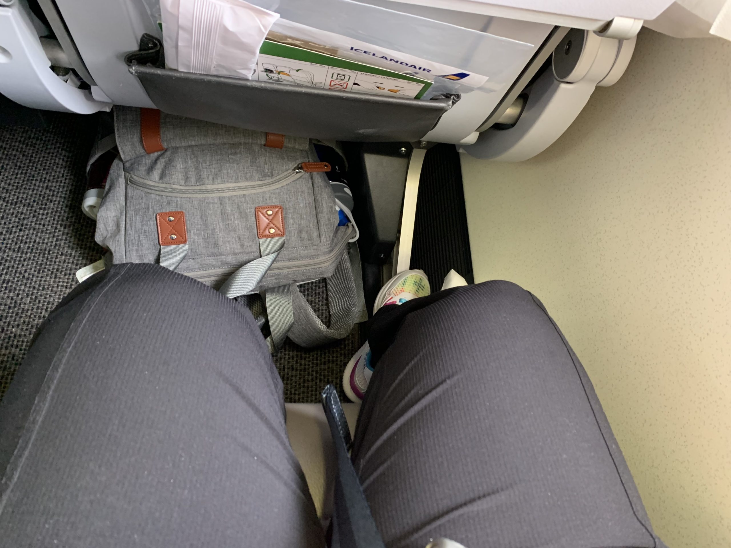 a person's legs and a backpack in an airplane