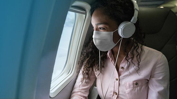 a woman wearing a mask and headphones looking out a window