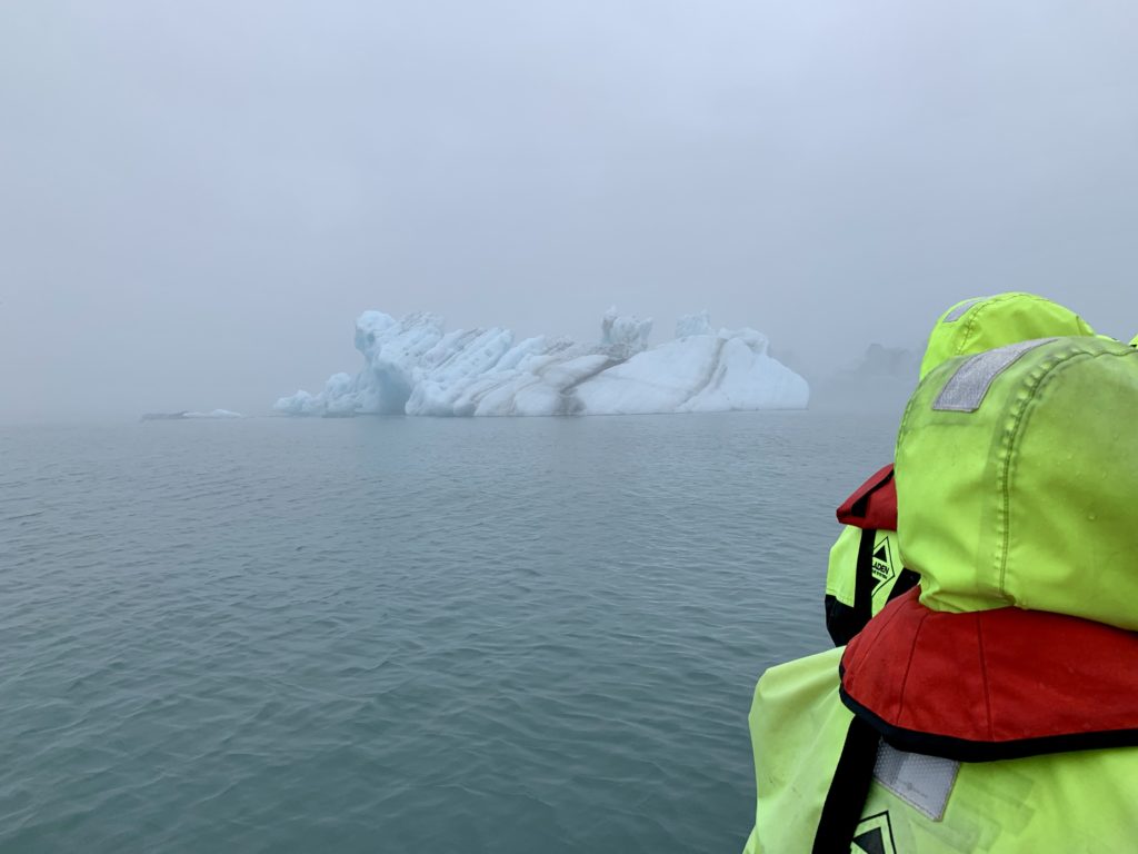 a person in a yellow jacket looking at an iceberg in the water