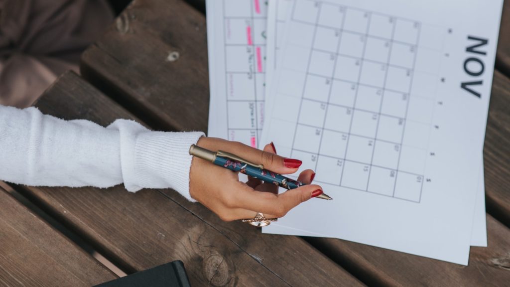 a hand holding a pen over a calendar