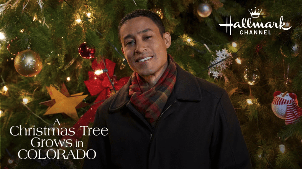 a man smiling in front of a christmas tree