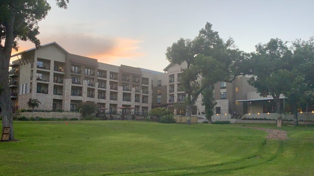 a large lawn with trees and buildings in the background