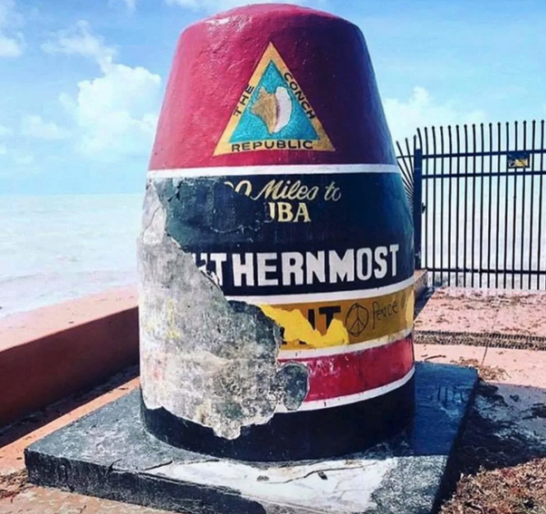 a red and white cone with a sign on it with Southernmost point buoy in the background