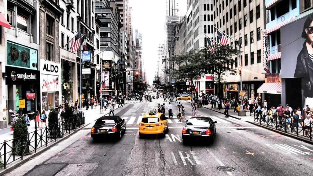 a group of people walking on a street with cars and buildings