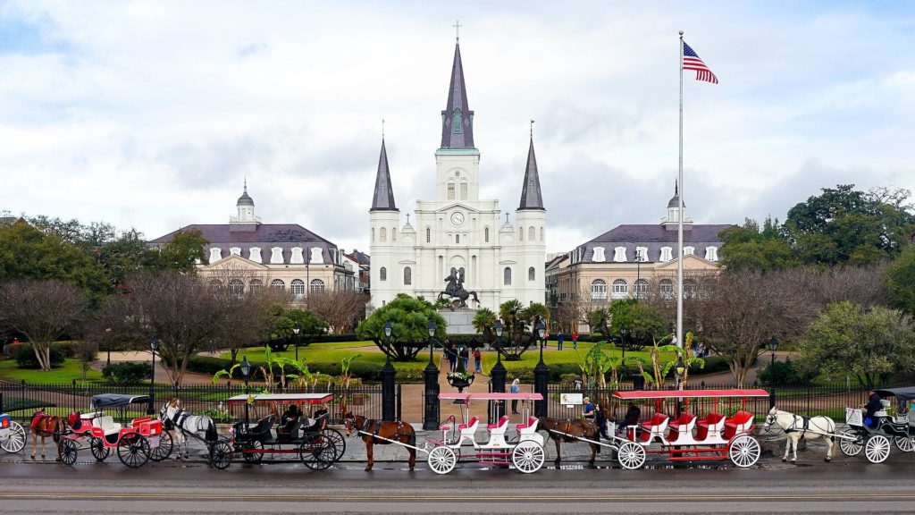 a horse carriage in front of a white building with Jackson Square in the background