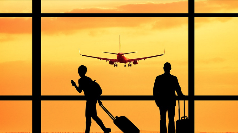 a silhouette of people with luggage and a plane flying in the sky