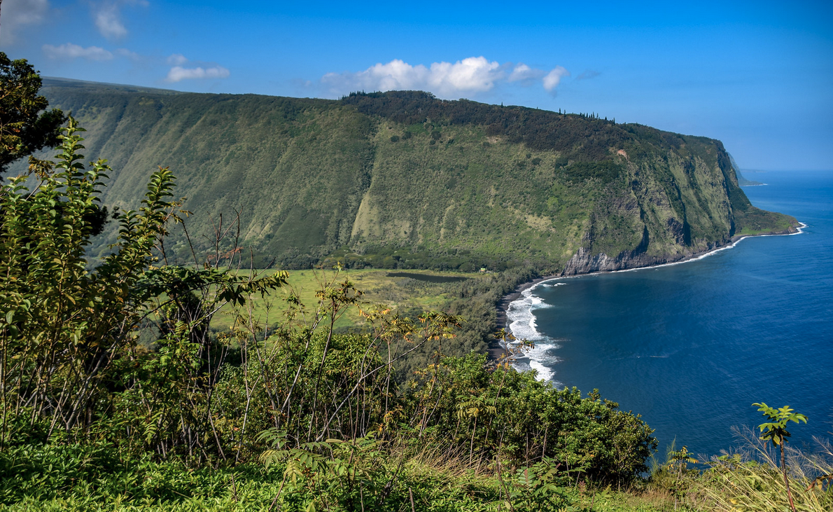 a green hills and a body of water with Waipio Valley in the background