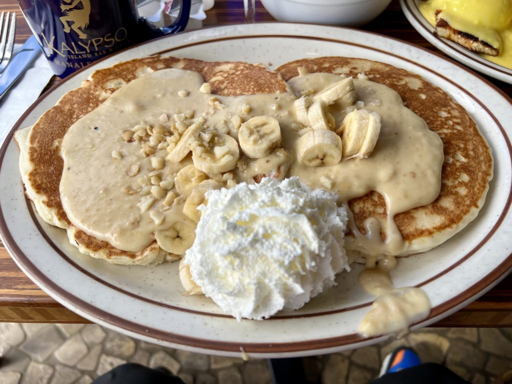 a plate of pancakes with bananas and whipped cream