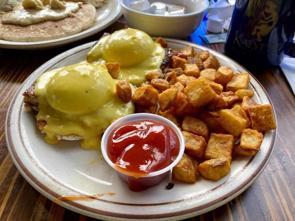 a plate of eggs benedict and potatoes