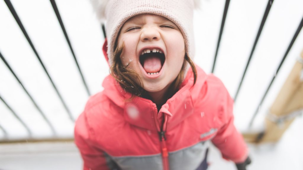 a girl in a pink coat and hat with her mouth open