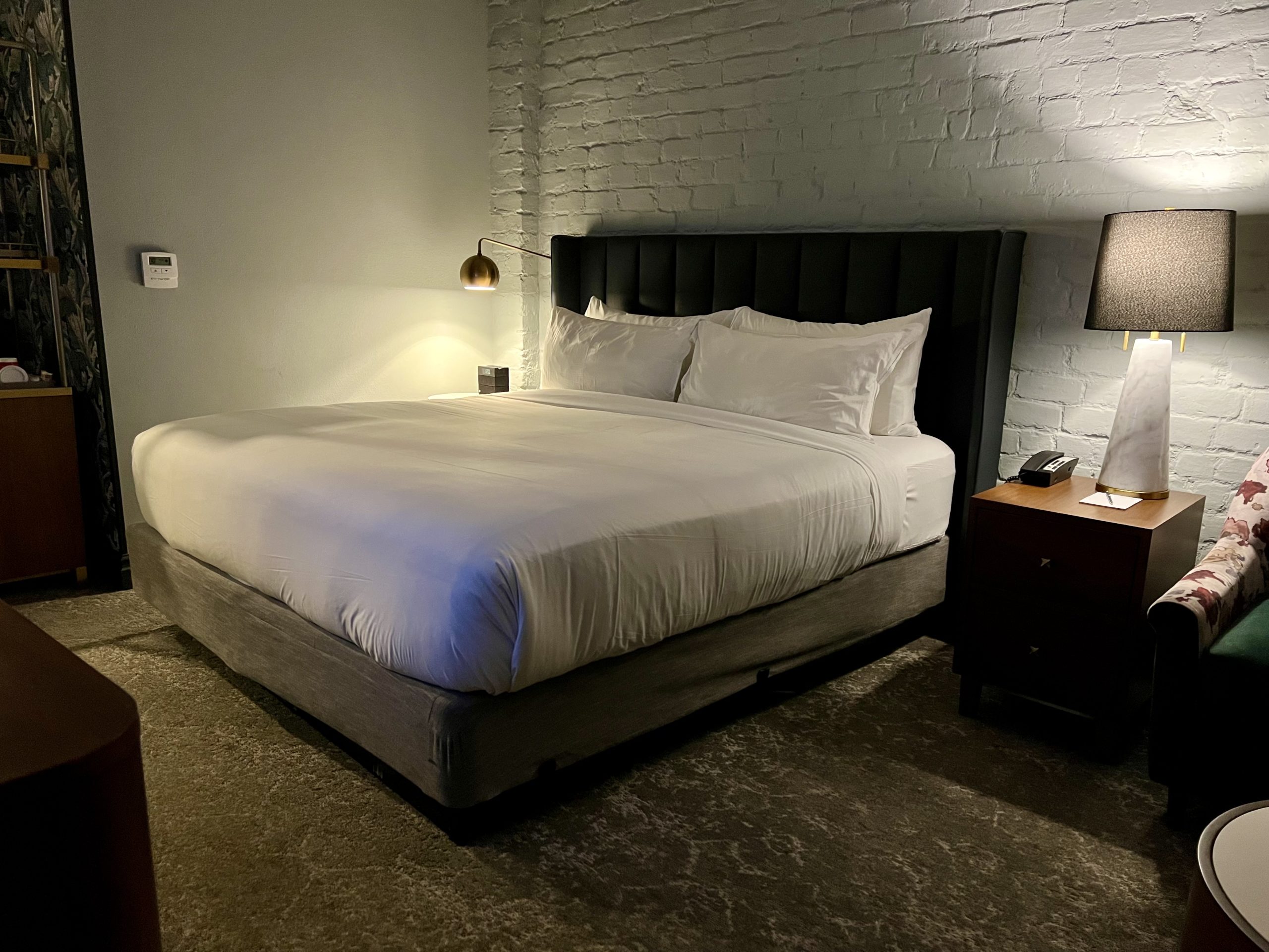 a bed with white sheets and a lamp next to a brick wall
