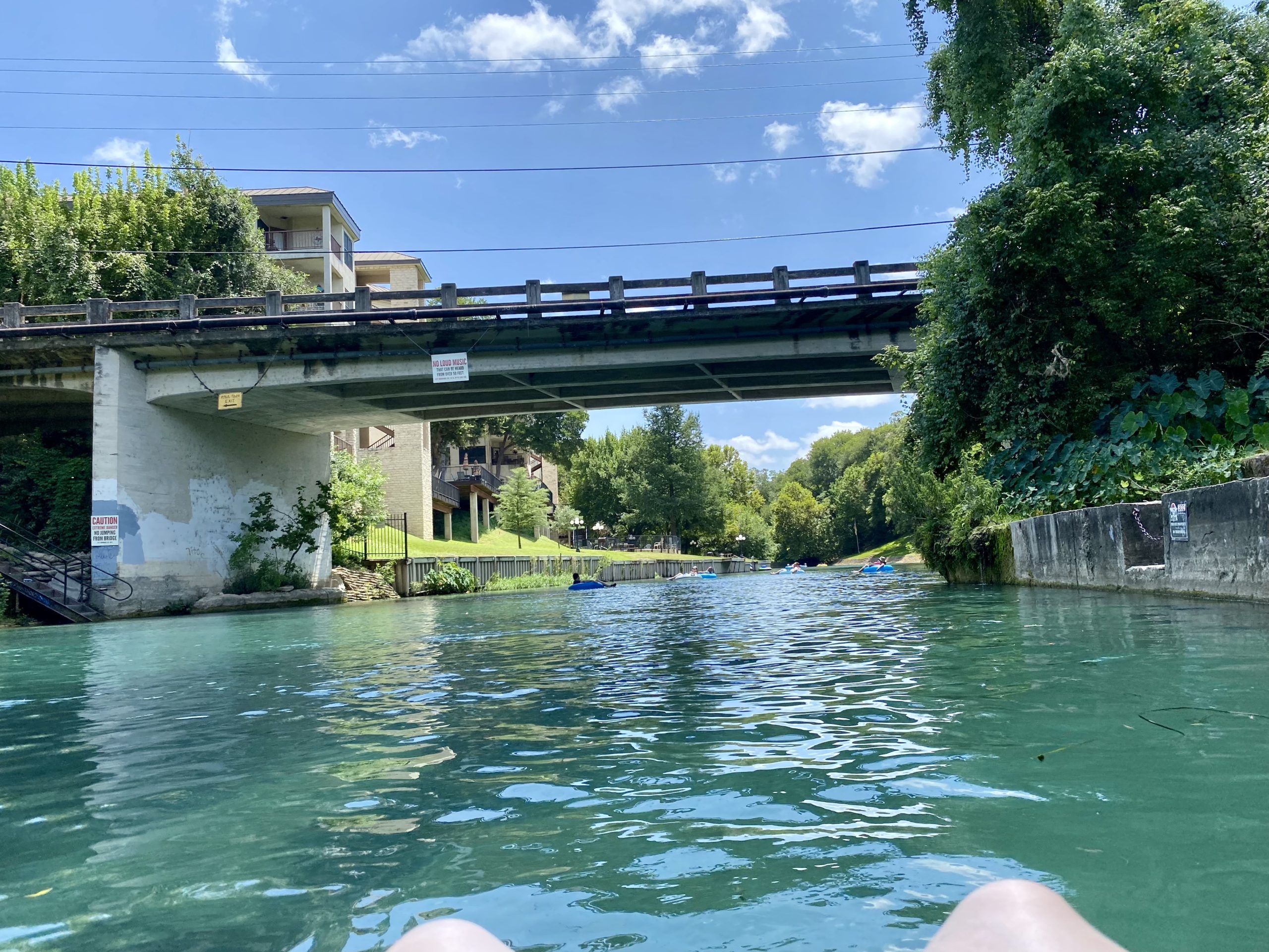 a person's feet on a body of water under a bridge