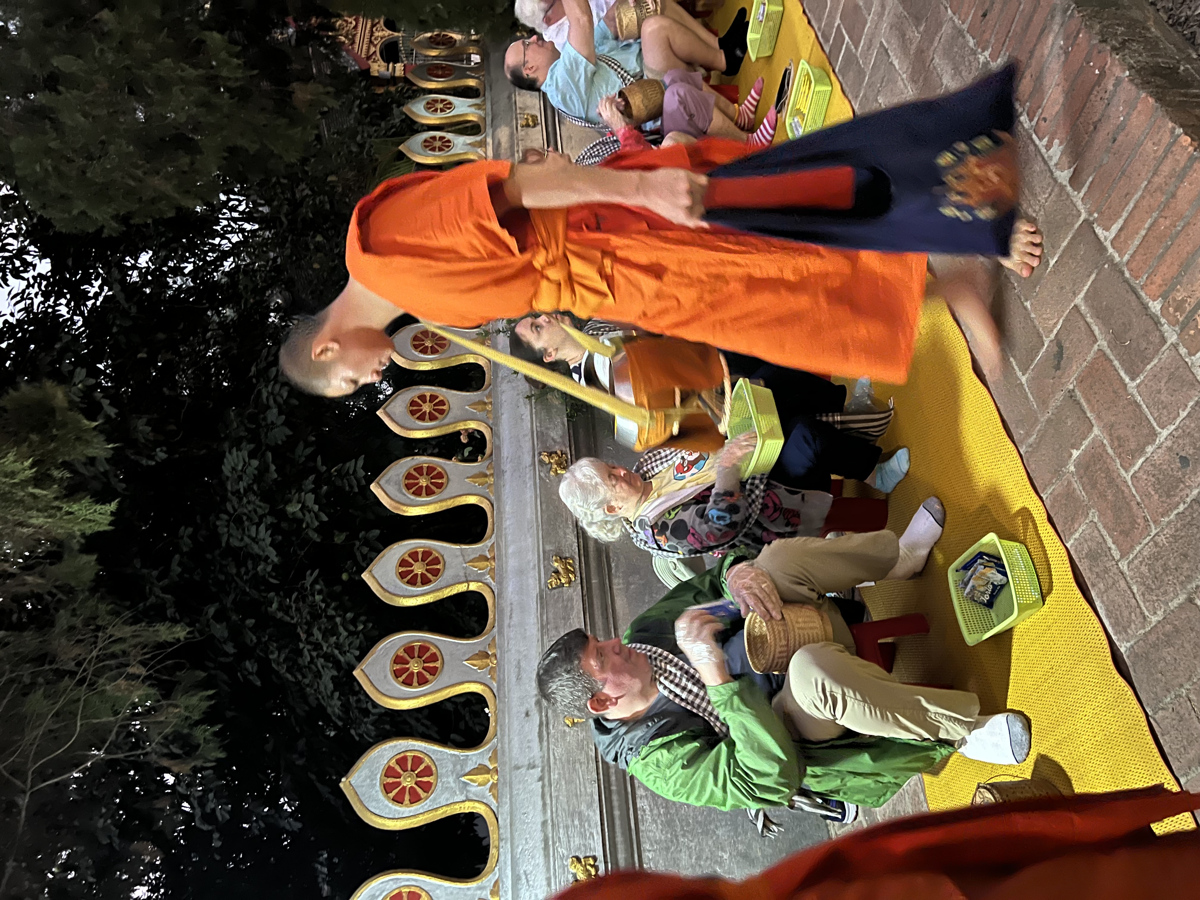 a man in orange robe standing on a yellow mat with people sitting on the ground