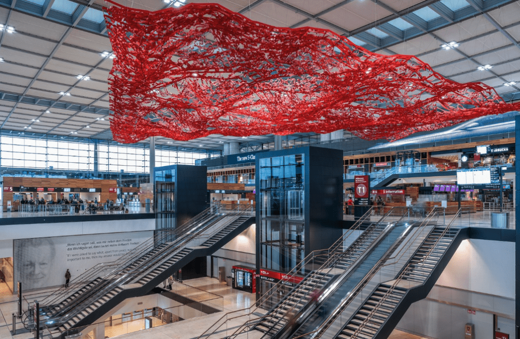 escalators in a building with a red sculpture from the ceiling