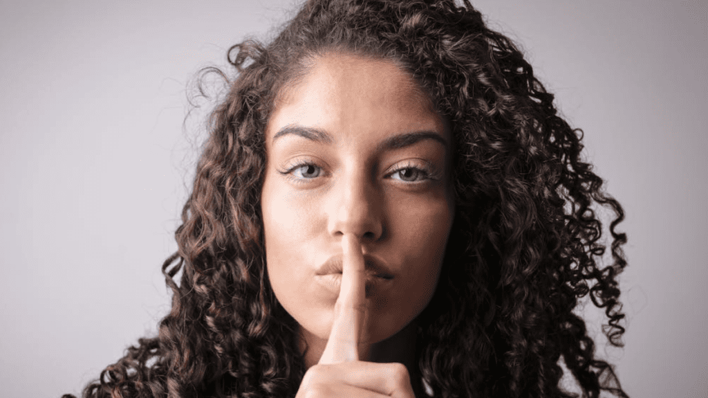 a woman with curly hair holding her finger to her mouth