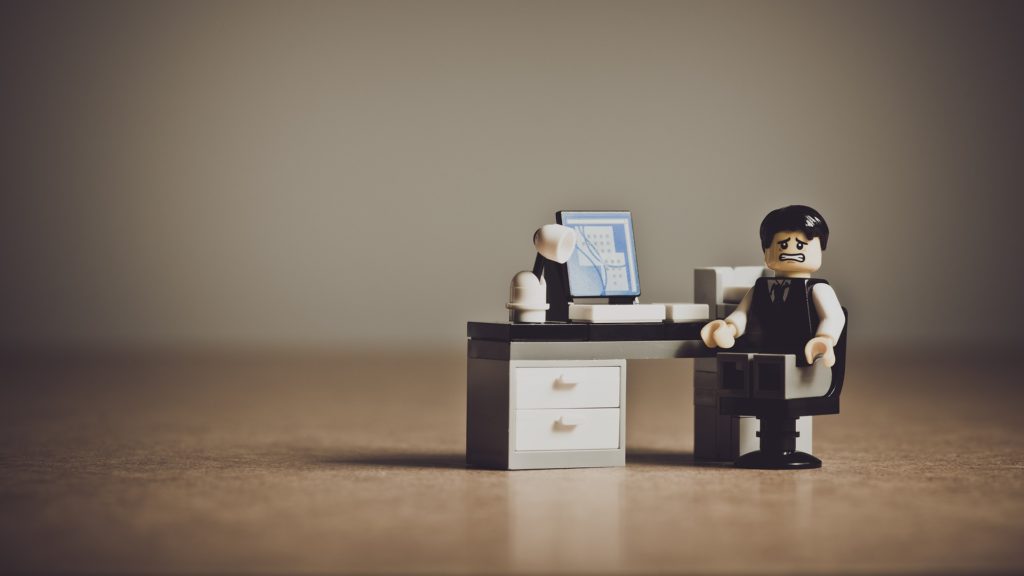 a toy figurine of a man sitting at a desk with a computer