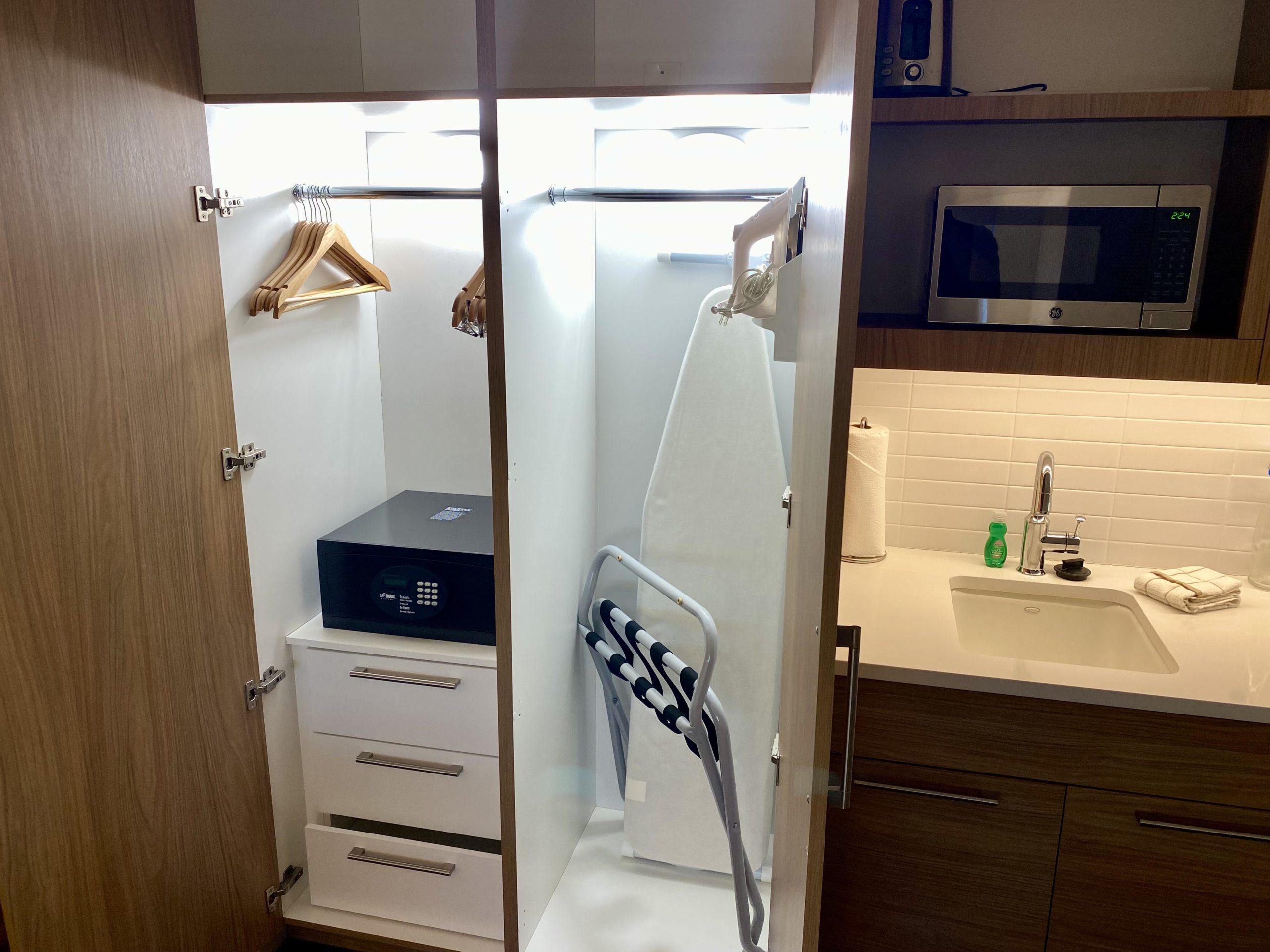 a closet with a white ironing board and a microwave