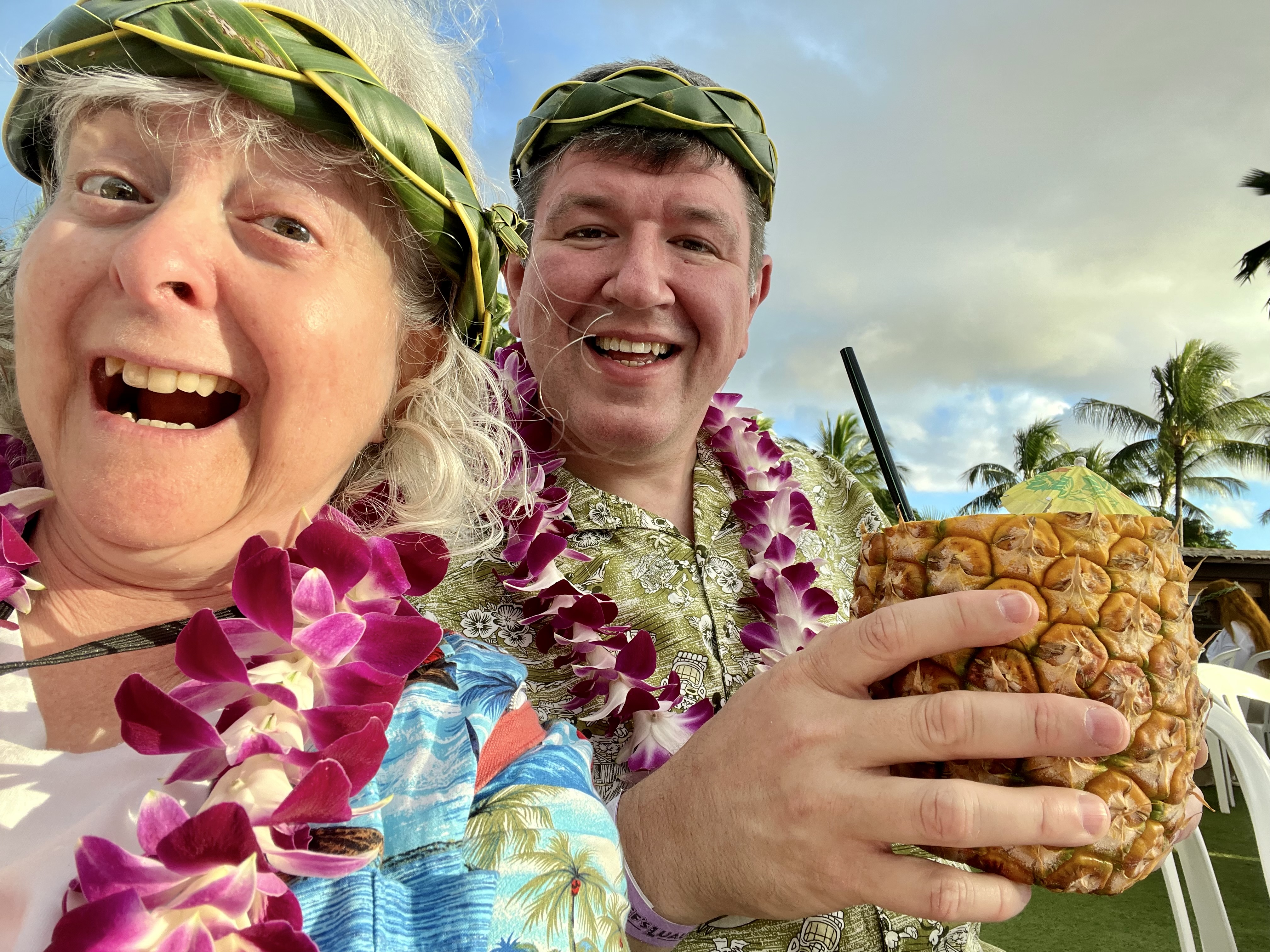 a man and woman wearing leis and holding a pineapple