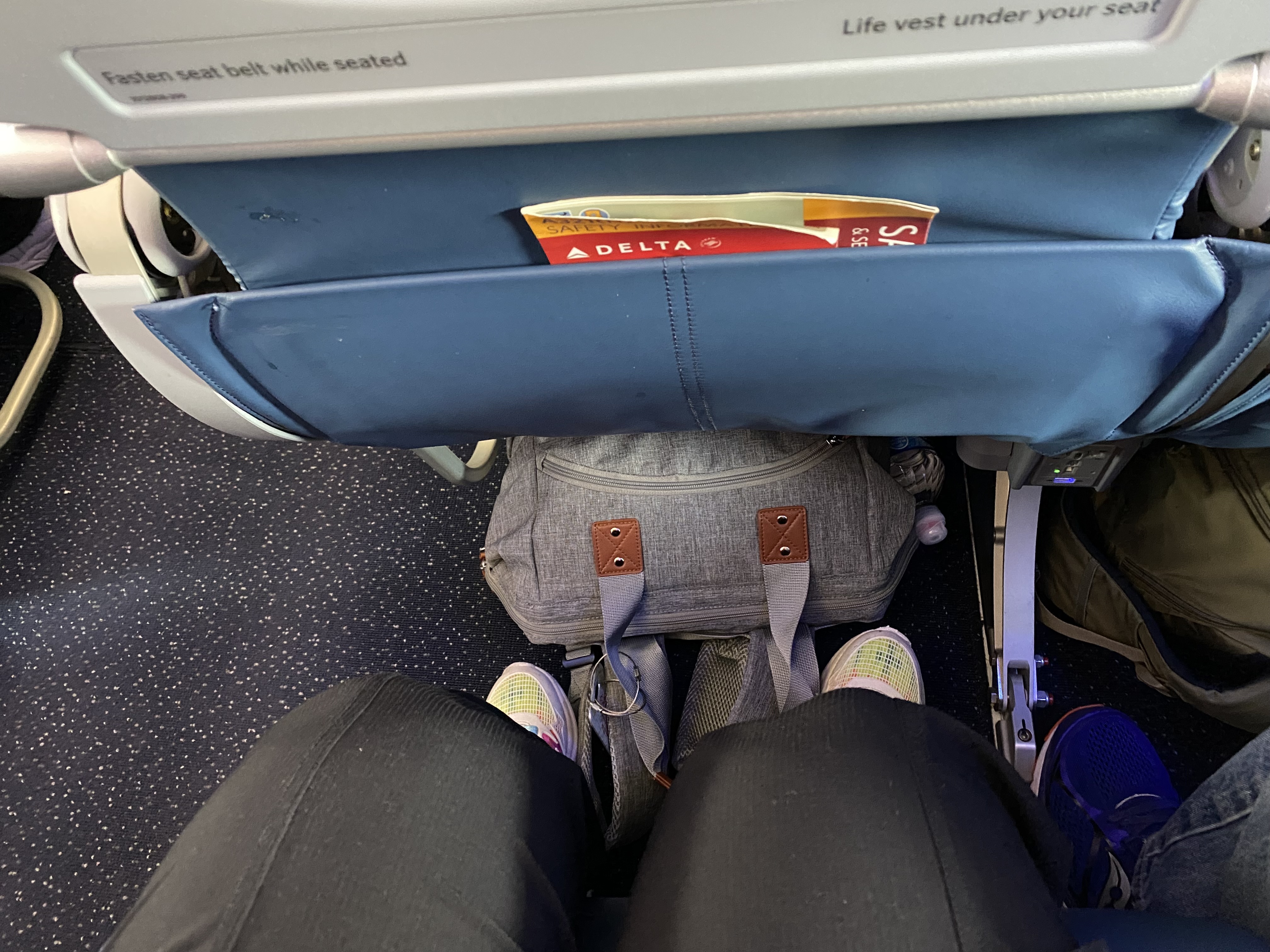 a person's legs and a bag in the seat of an airplane