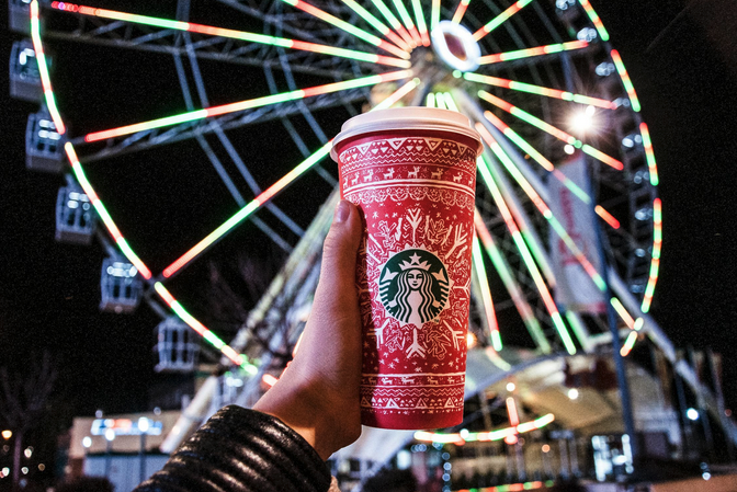 a hand holding a red cup with a white lid and a red ferris wheel in the background